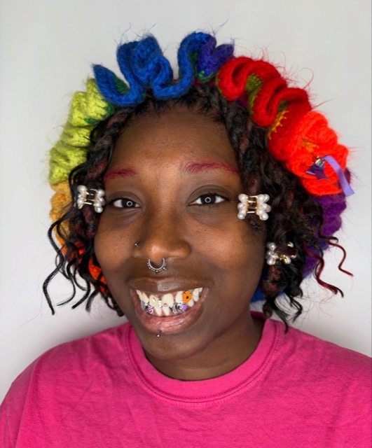 Beaming client with rainbow hair showing a set of colorful tooth gems including a flower motif