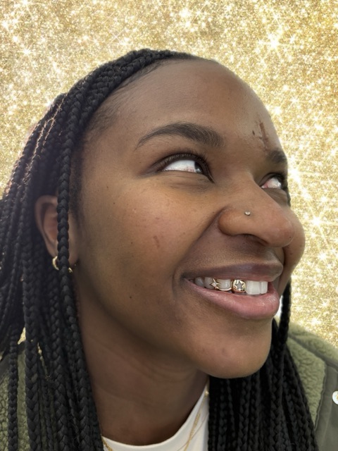 Client with box braids smiling against a gold sparkle backdrop, showing a gold-framed crystal tooth gem