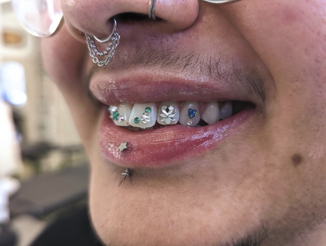Close-up of crystal tooth gems across the upper teeth, worn with paired lip piercings