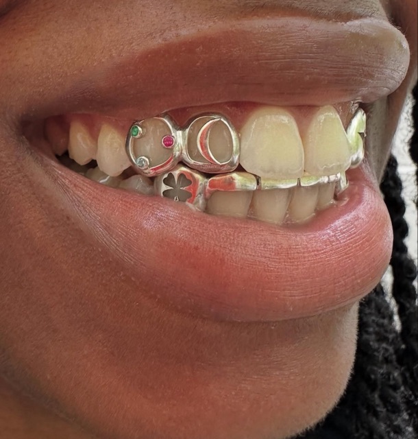 Close-up of open ring and flower tooth jewelry set across the upper teeth alongside braces