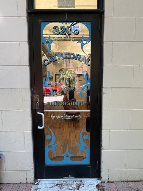 The studio's front door at 3205, glass painted with blue designs and lettering reading Cathedral Tattoo Studio, by appointment only