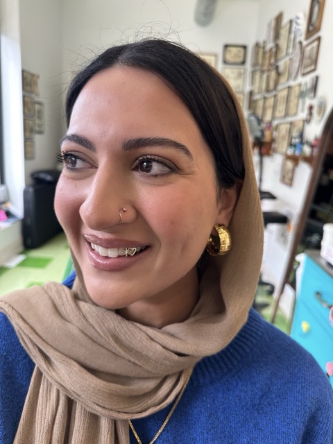A client smiling in the studio after an appointment, showing gold tooth jewelry, with the studio's framed art behind her